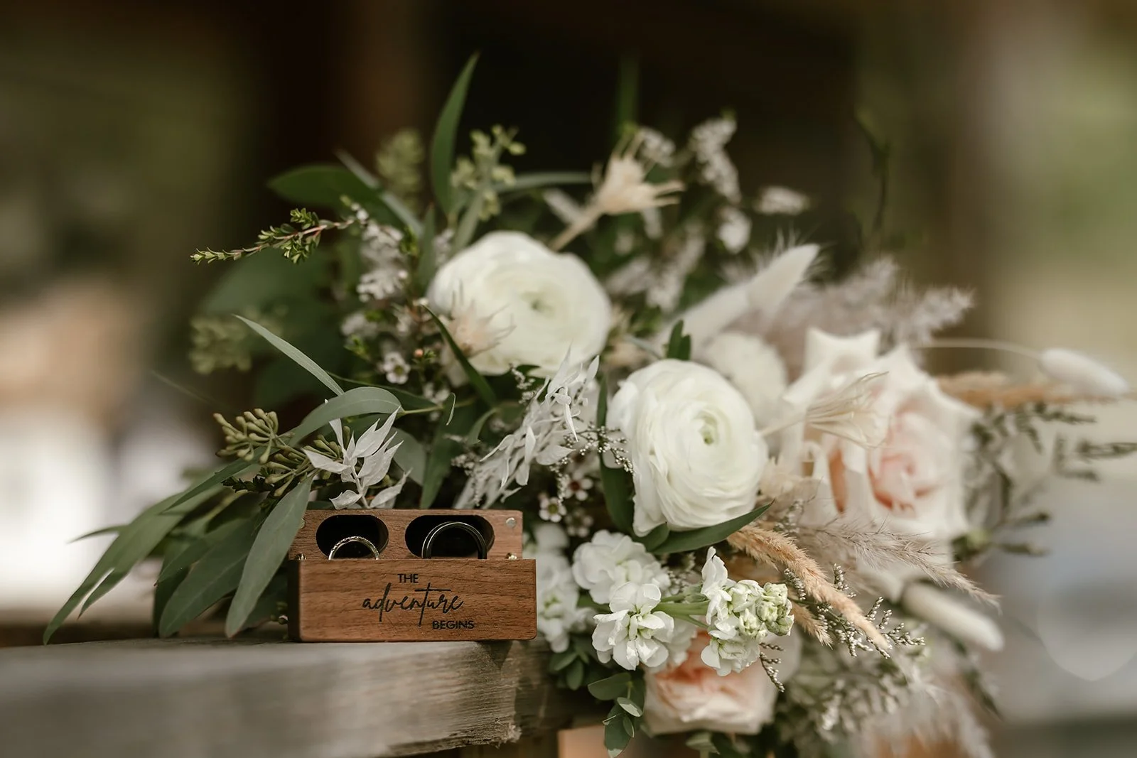  A beautiful bouquet of wedding flowers with a wooden box with rings along side of them.  