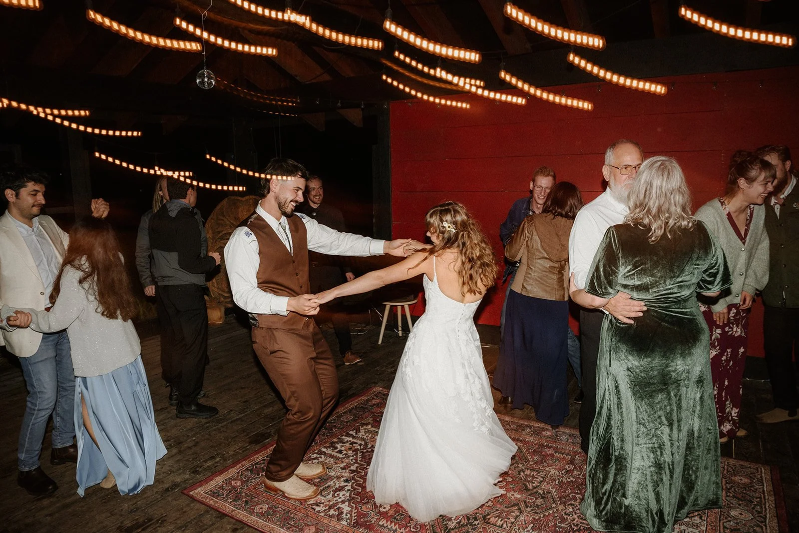 A bride and groom dancing outside at night with wedding guests around them and lights above.  