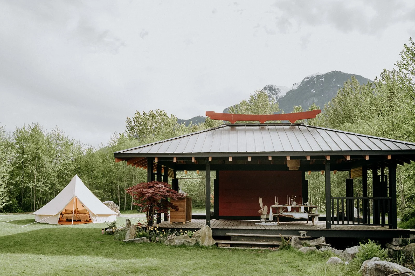  A japanese structure with a large white tent alongside of it in a beautiful green setting at Cheekye Ranch. 