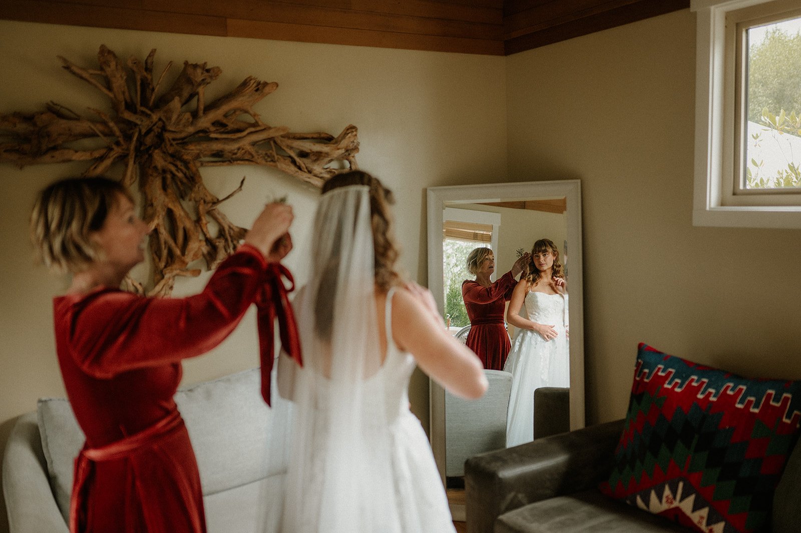  A bride getting ready in a building with another woman in red putting on her veil. 