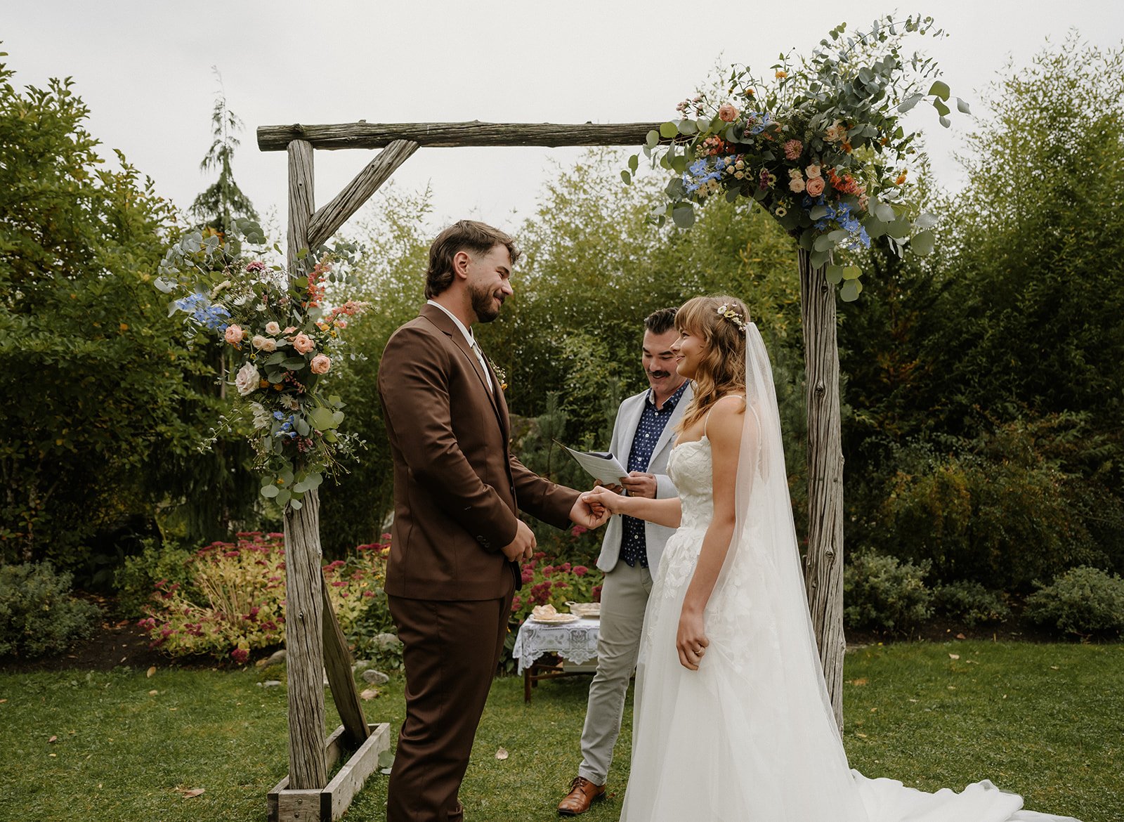  A bride and groom in front of a wood structure with flowers and greenery in the background. 