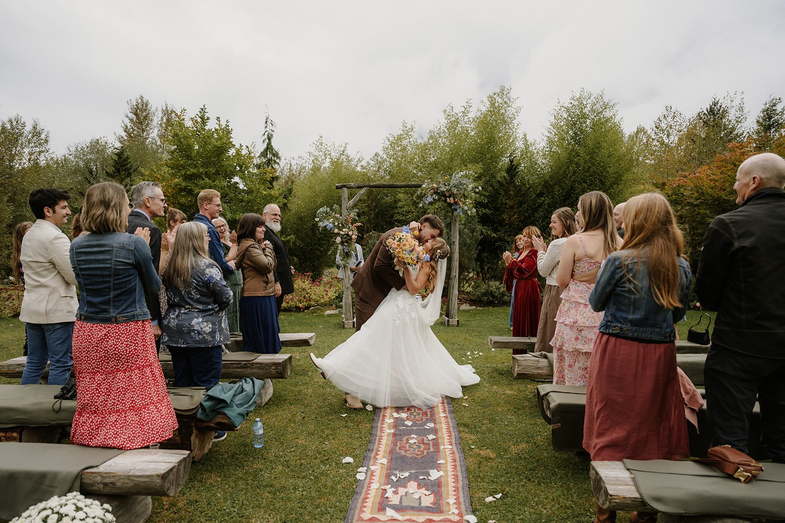  A bride and groom kissing down an aisle with wedding guests on either side at Cheekye Ranch. 