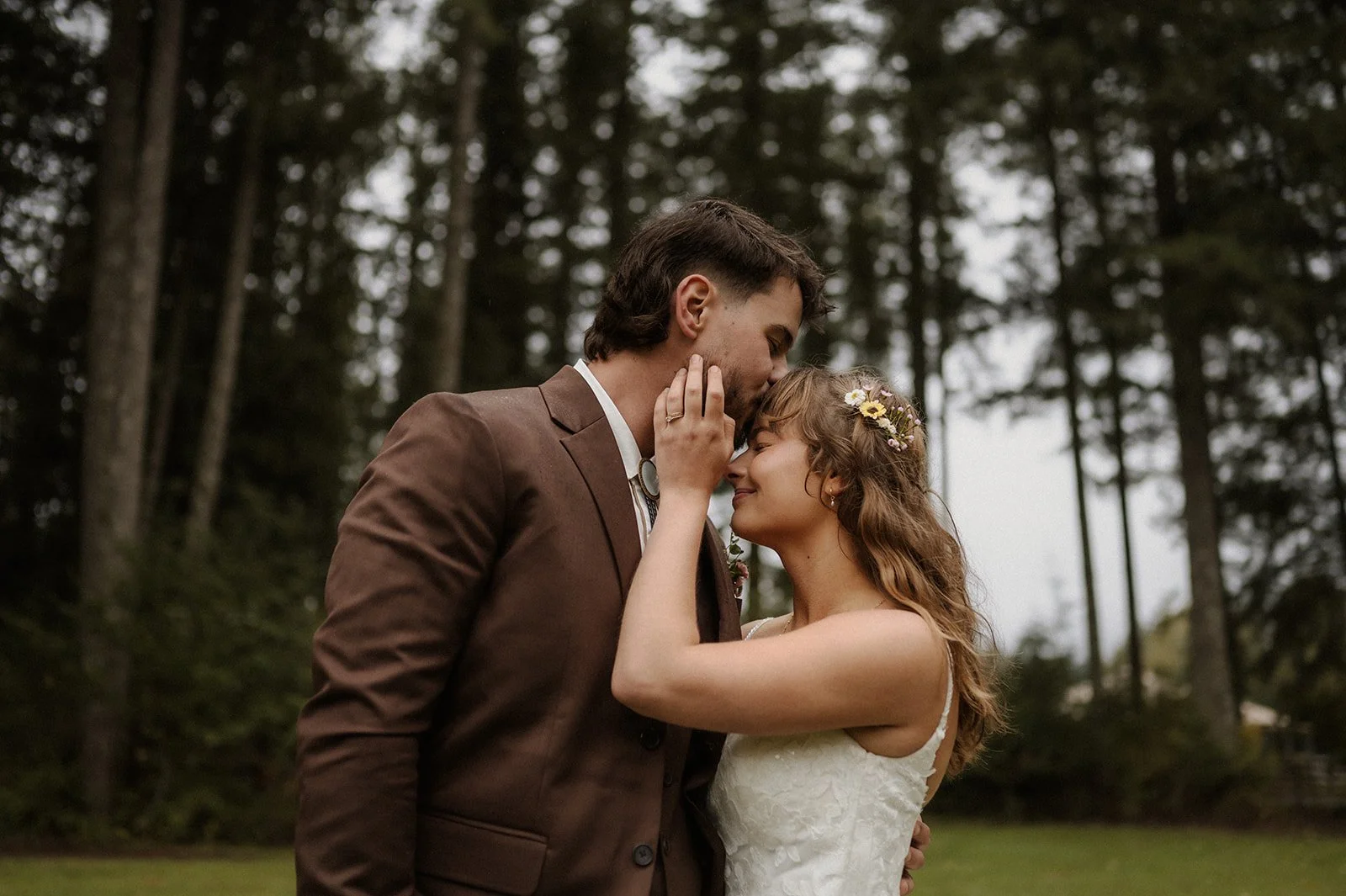  A bride and groom in a close embrance with tall trees behind them.  