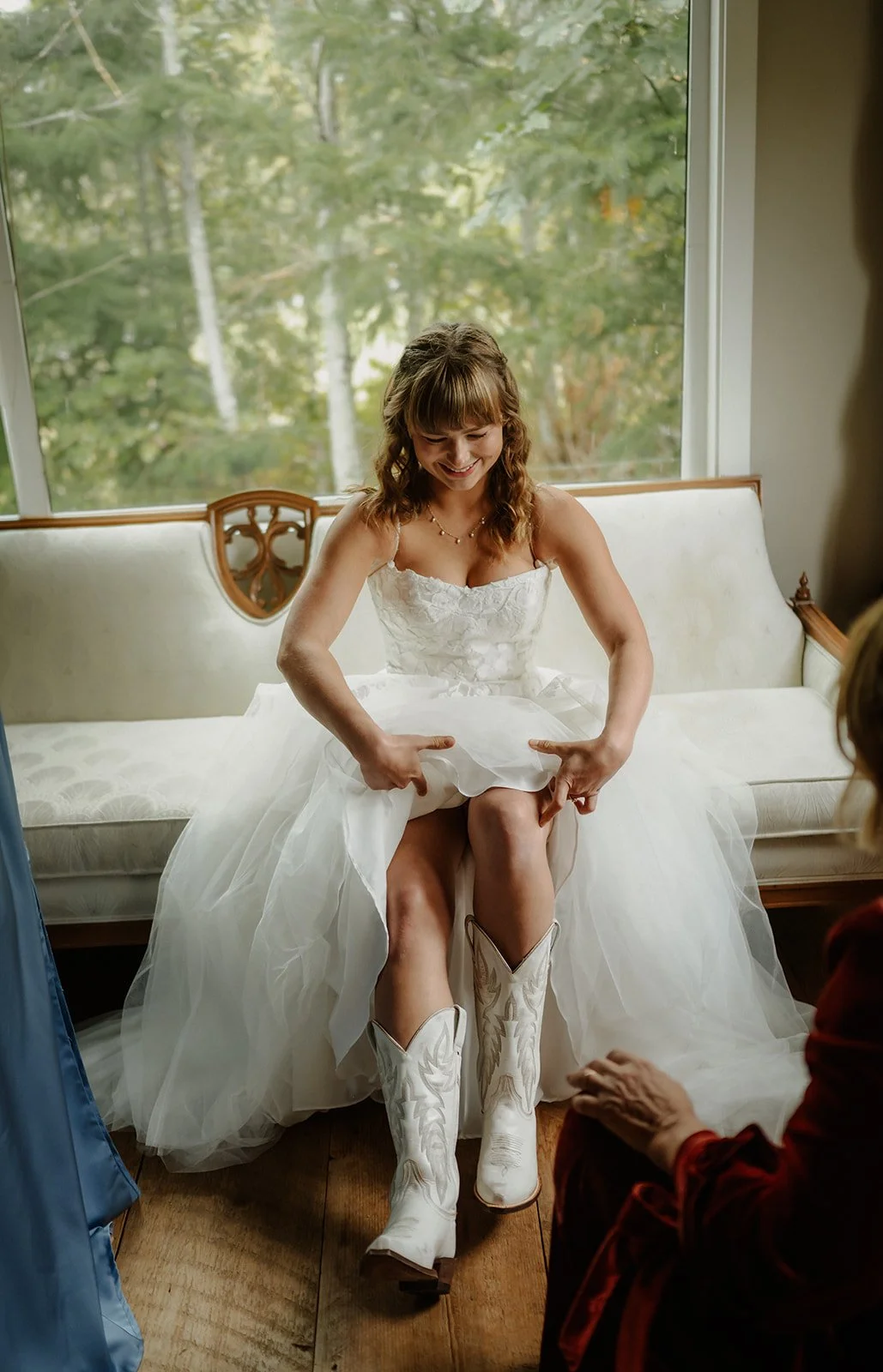  A bride getting ready and putting on white cowboy boots while sitting down.  