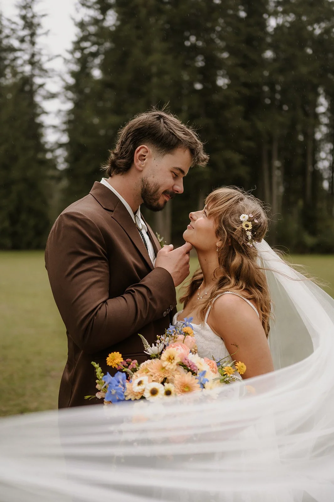  A bride and groom looking at each other with trees in the background and a veil in front of them.  