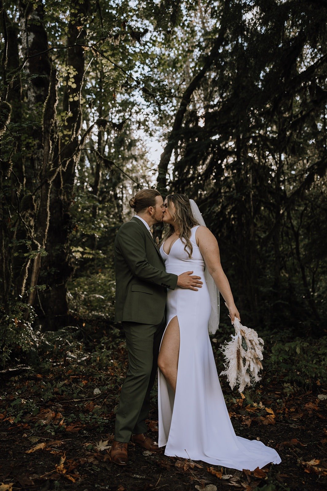  A bride and groom kissing each other in a beautiful forest setting with the sun peeking through.  
