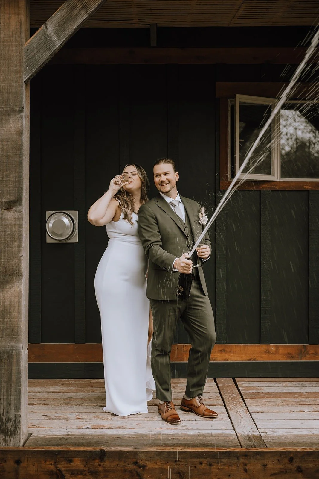  A bride and groom standing on a porch and spraying champagne.  