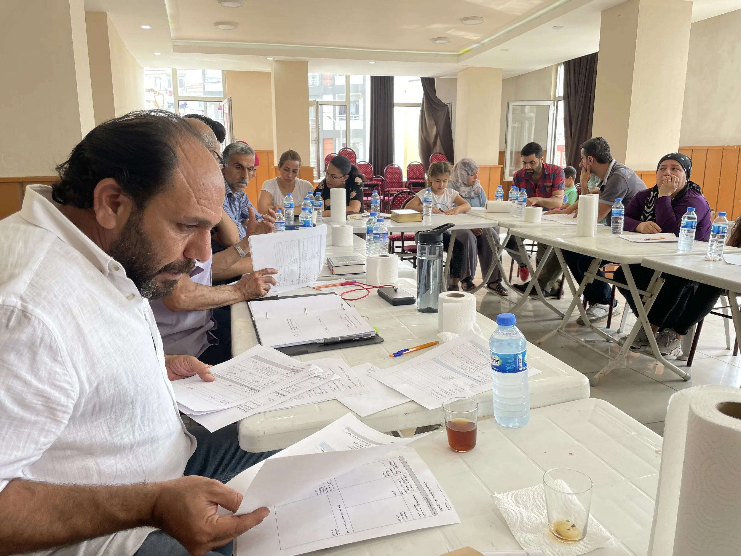 People sitting around a table in a bright room, reviewing documents and drinking beverages.
