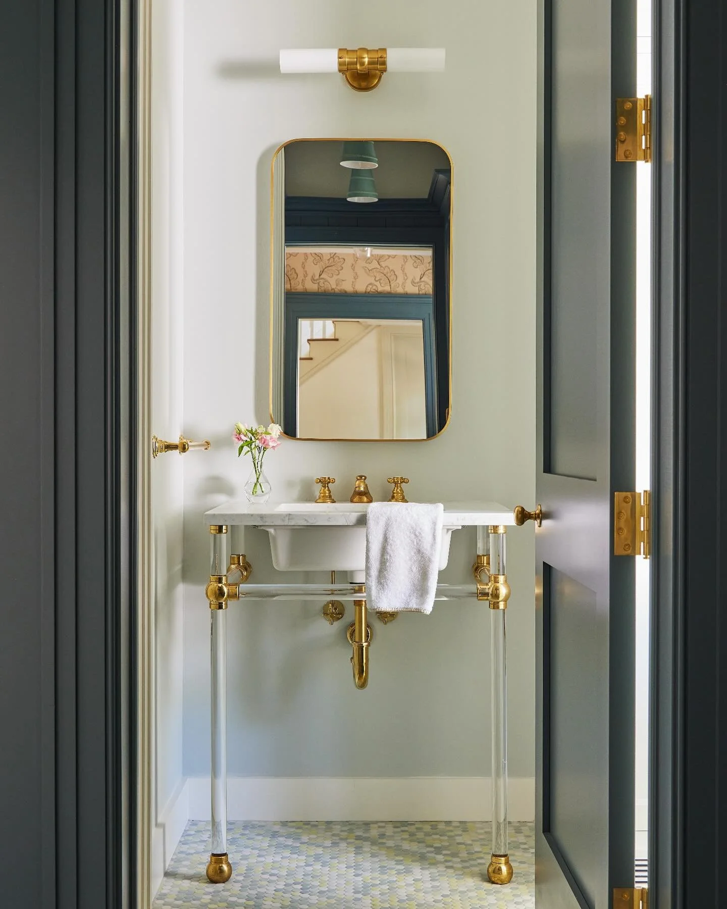 For the powder room off the mudroom at our #Greenwich project, we put a playful spin on traditional design, with a multi-color pennytile, brass accents, and acrylic vanity legs. Photo: @katesjordan