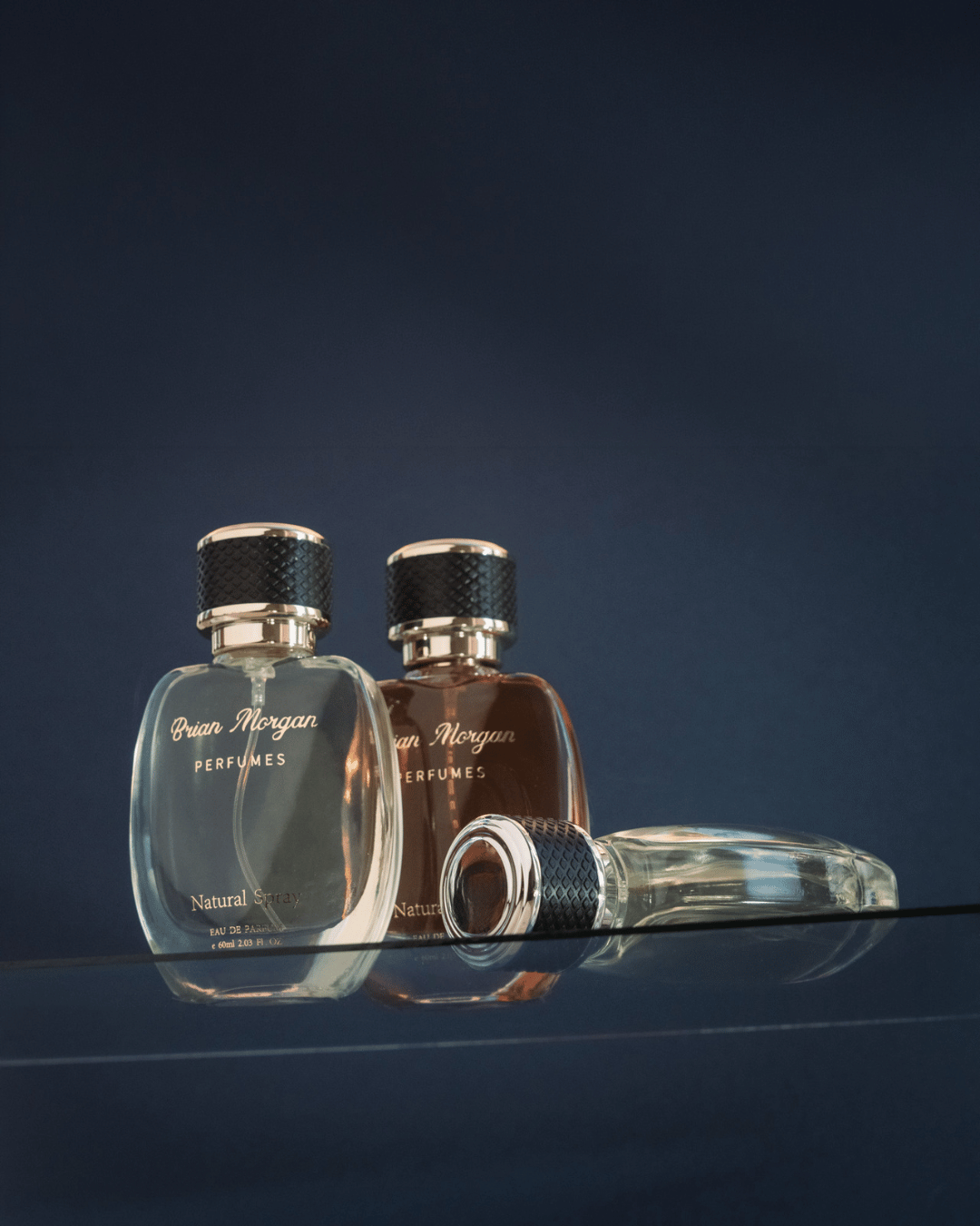 Three Brian Morgan perfume bottles, two upright and one lying down, against a dark background with reflective surface.