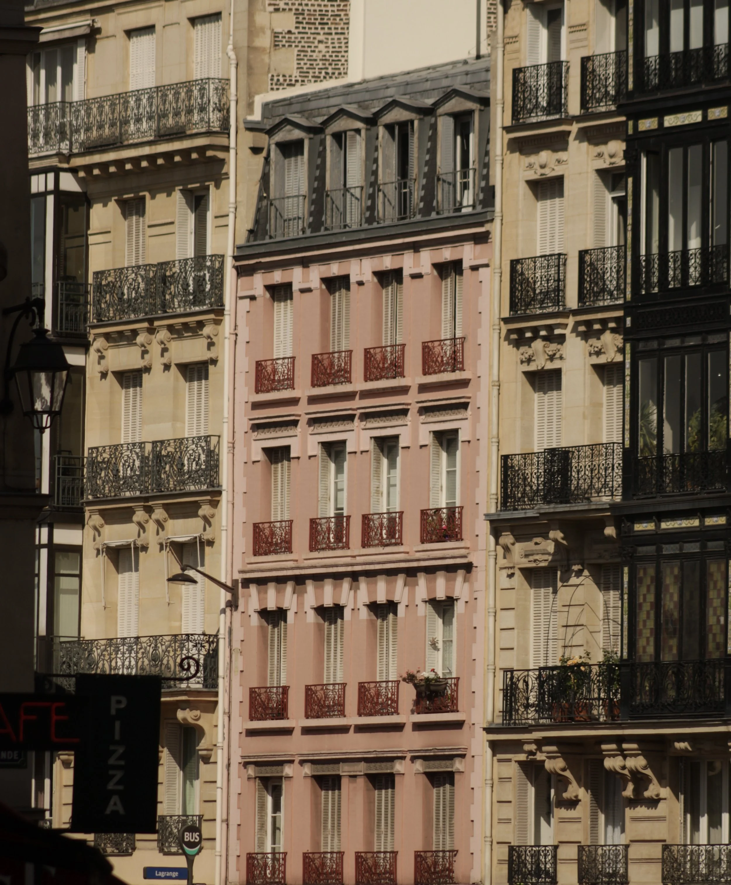 Multi-story apartment building with ornate black, red, and gray balconies and shutters, and other buildings visible in the background.