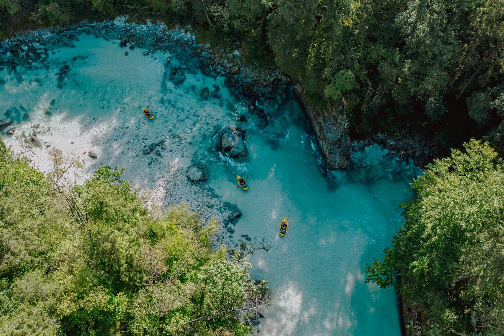 Quatre packraft jaunes navigant sur la rivière Soča en Slovénie, l'eau est bleue turquoise entourée d'arbres verts.