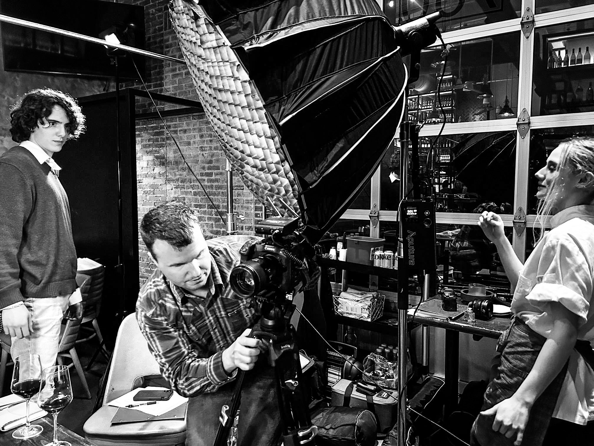 Group of people in a restaurant setting with a camera and lighting equipment, likely filming or photographing.