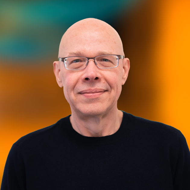 A man with glasses and a bald head is smiling, wearing a black shirt, with a blurred colorful background.