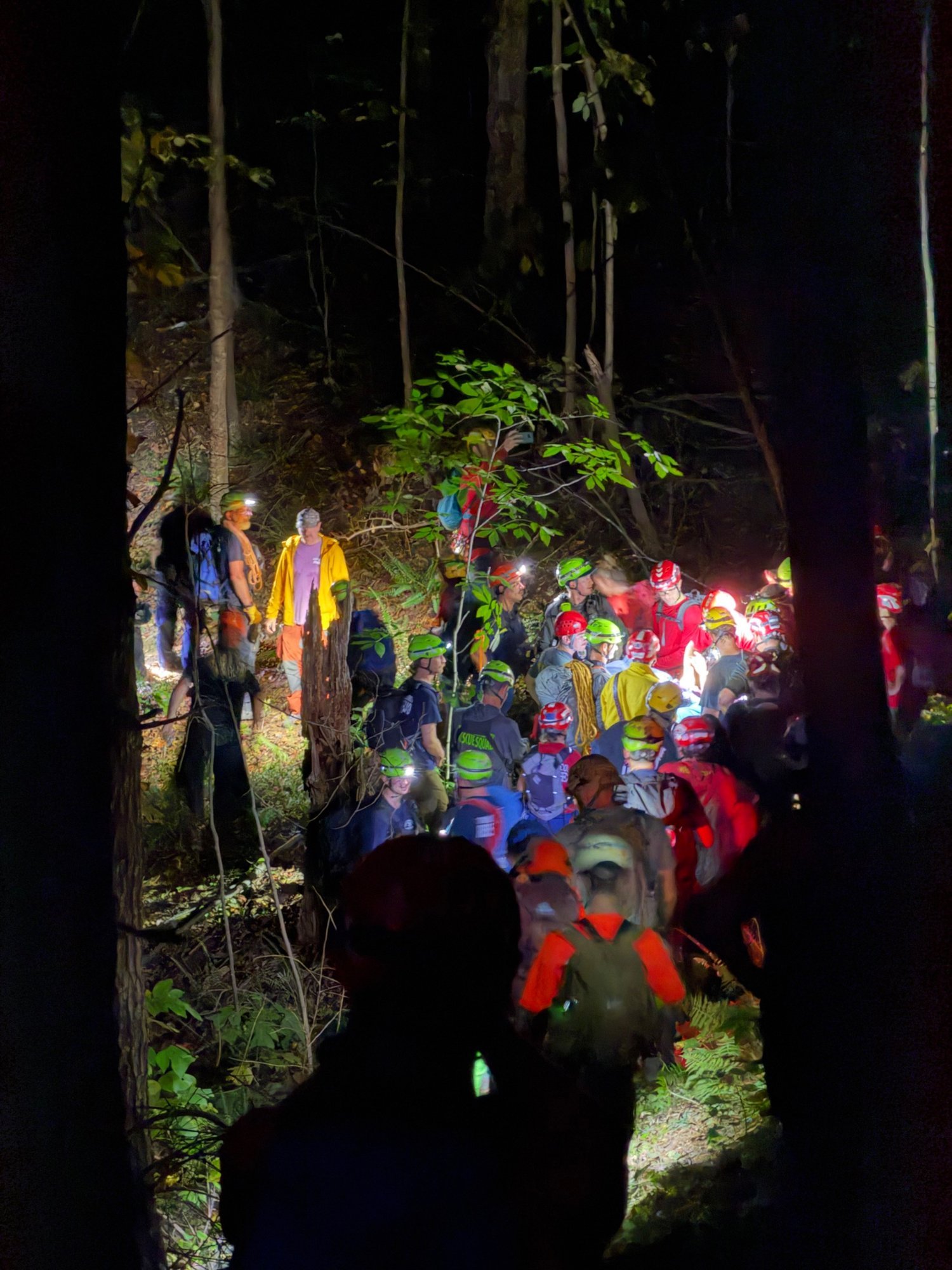 Large group of rescuers in helmets and headlamps carrying a litter through the woods at night in Western North Carolina.