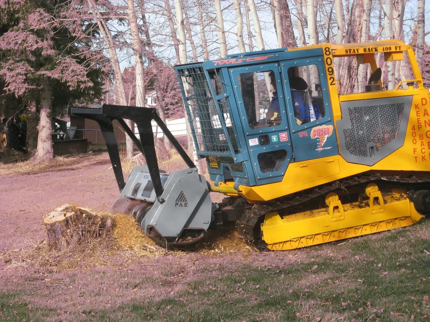 Tracked mulching machine grinding a tree stump along a wooded access path