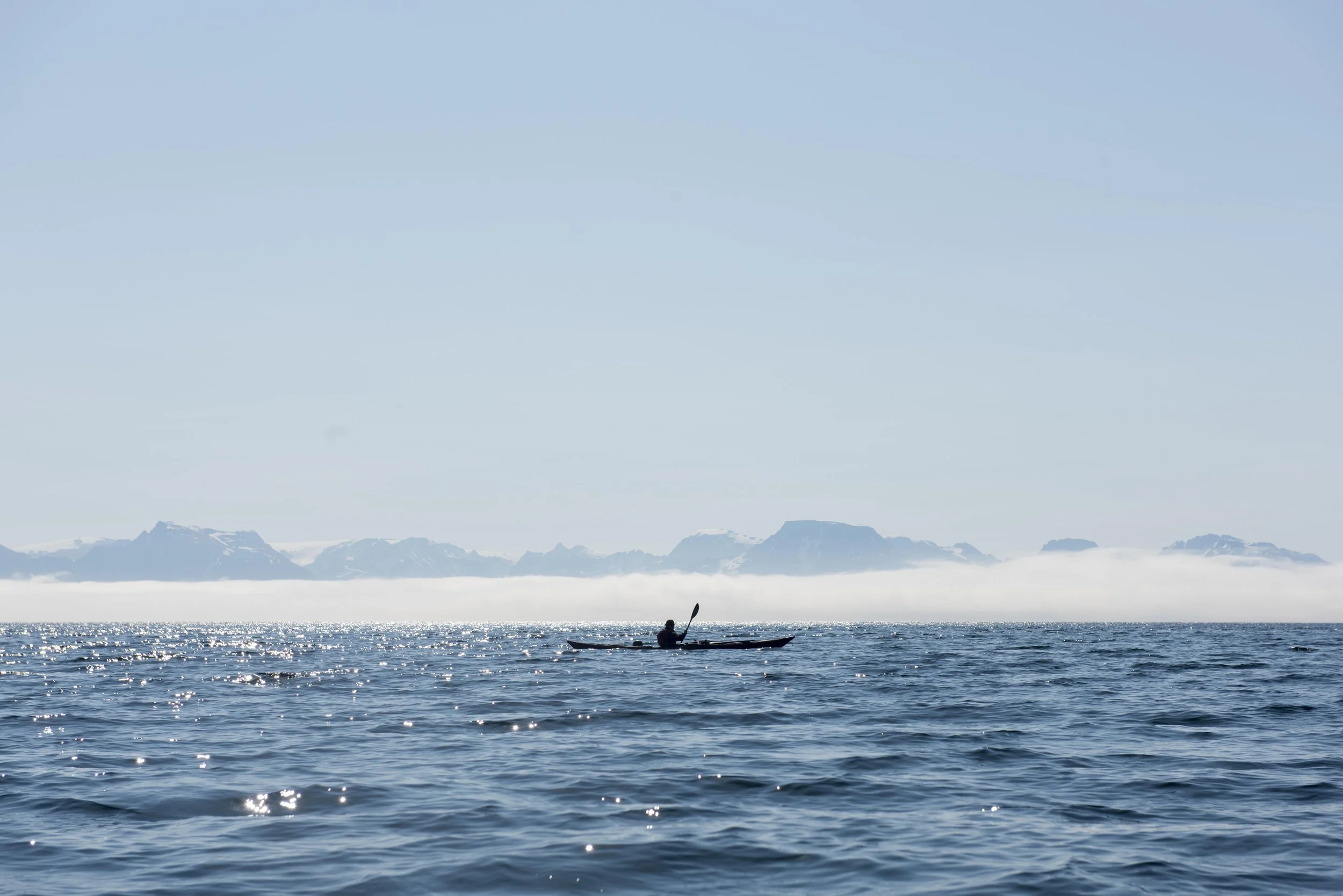 Lone sea kayaker off Sørøya looking towards mainland Norway with a fogbank on the horizon
