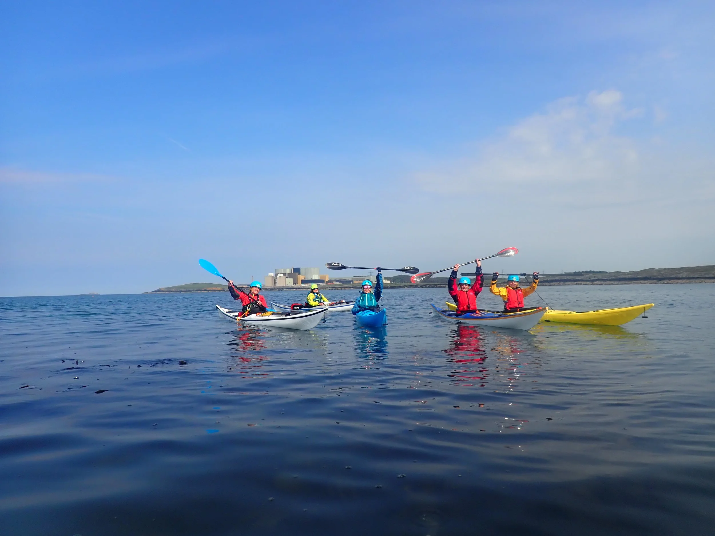 5 Kayakers in colourful boats on the sea off the Anglesey coast with a sea kayaking wales guide