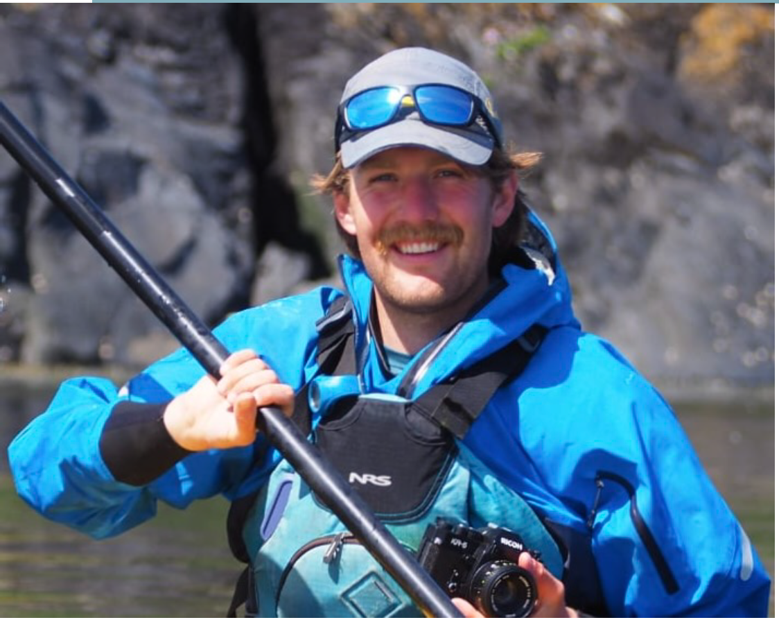Sea Kayaking Wales Kayak Coach in Blue kayaking cag holding a black paddle