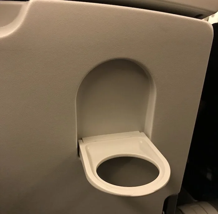 Stowed tray table with embedded cupholder folded down, ready for use.