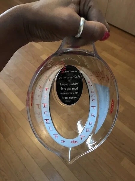 Picture of my brother’s clear, plastic measuring cup (from the top) with a label that reads, “angled surface lets you read measurements from above.”