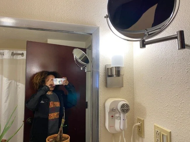Image of the two-sided mirror attached to a metal arm that’s been drilled into the wall and myself in comparison to its height.