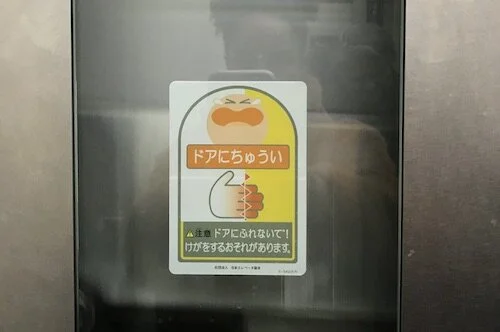 Picture of a sign in Japanese with a cartoon showing a face in pain and a hand seemingly injured and stuck in between sliding panels.