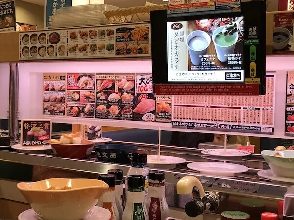 Image of the sushi menu along with plates of sushi on a conveyor belt.