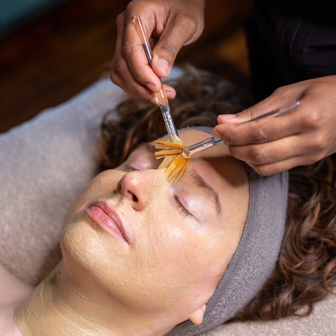 A person receiving a facial treatment with facial extraction tools and a facial mask applied.