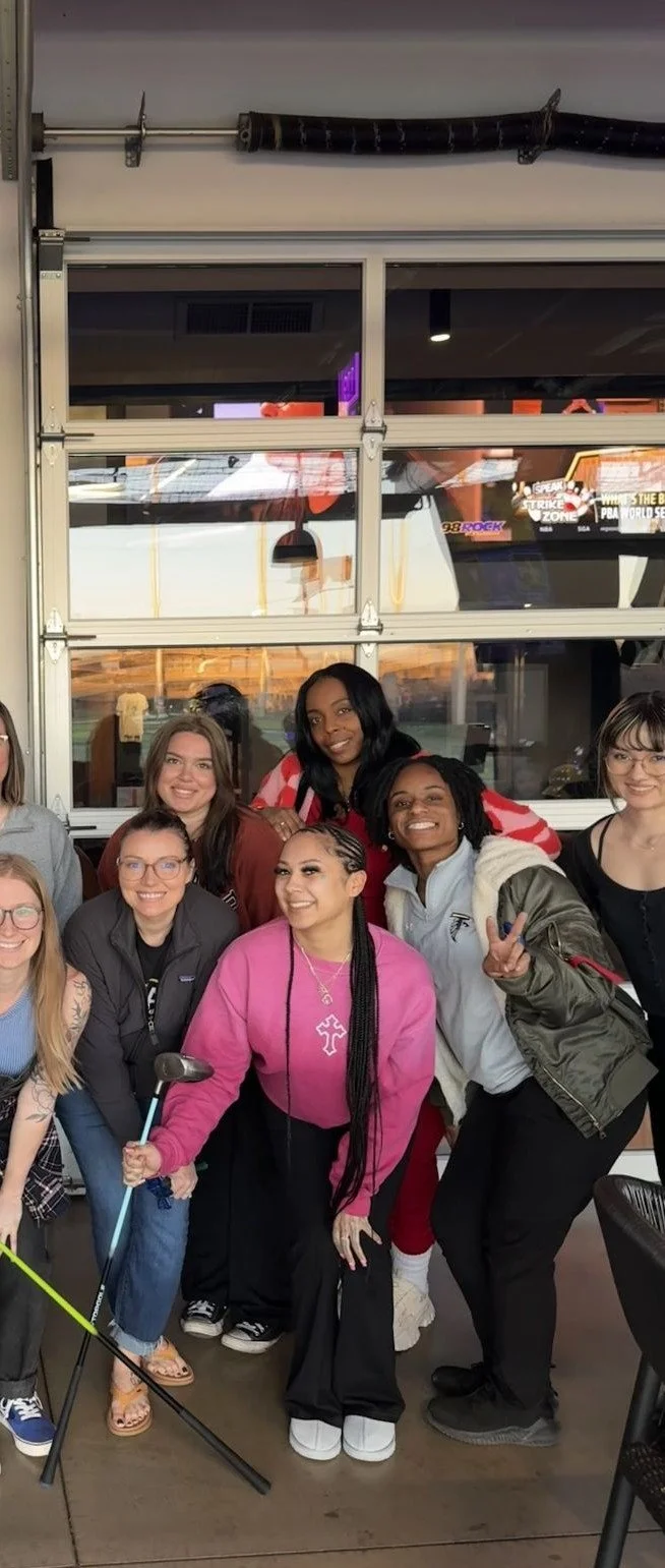 Group of women smiling and posing for a photo in an indoor venue with a garage door behind them.