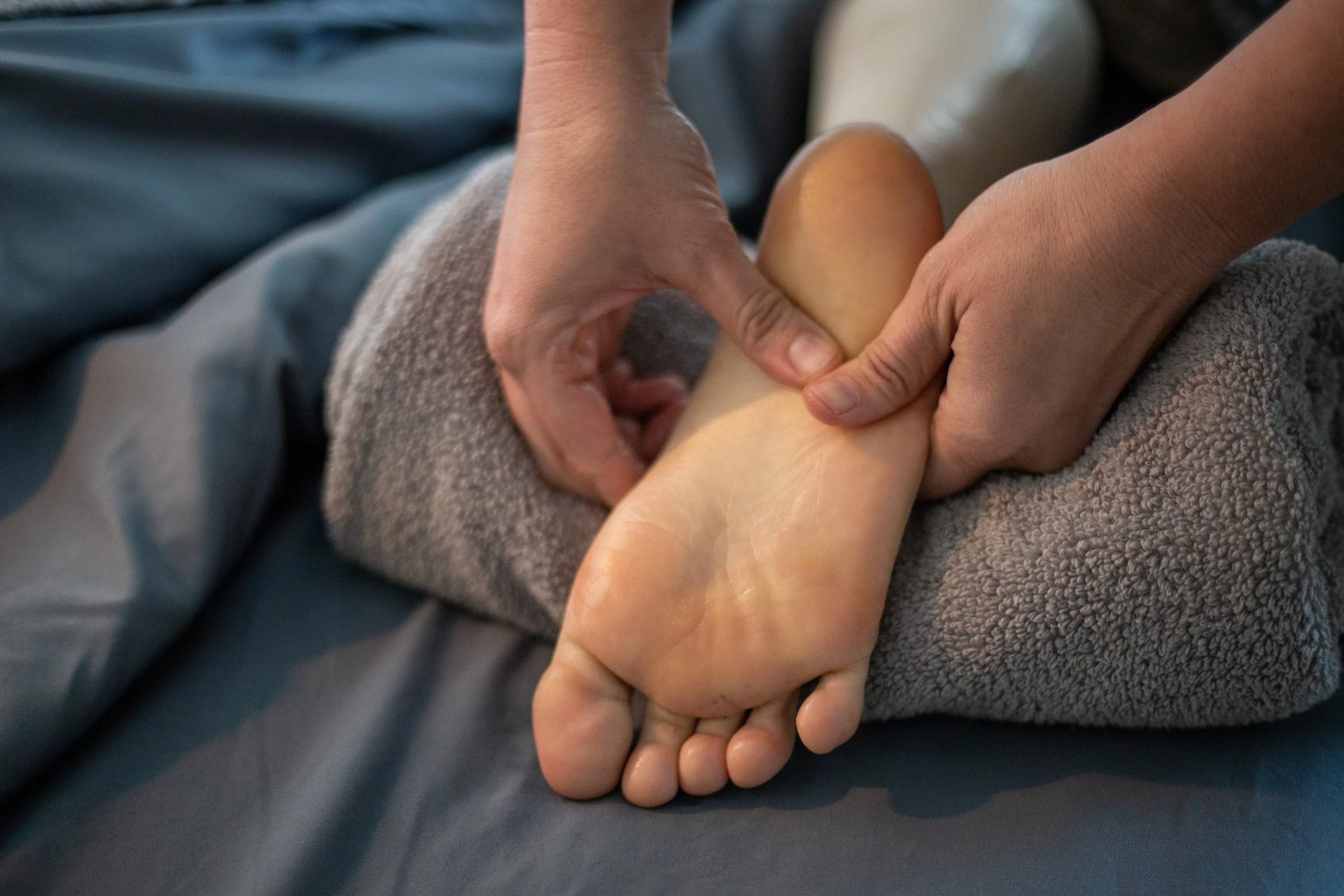 Close-up of two hands giving foot massage to a person's foot resting on a gray towel.