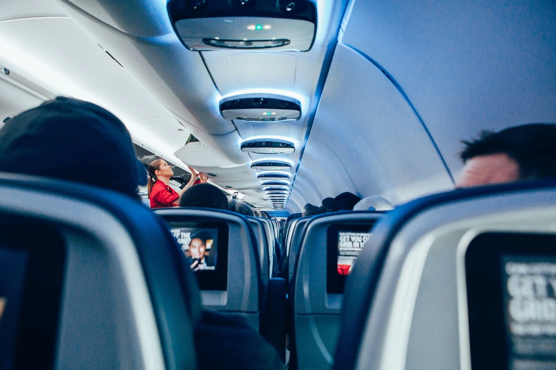Passenger seated in an aeroplane with a cabin crew member stood up next to an open overhead luggage container.
