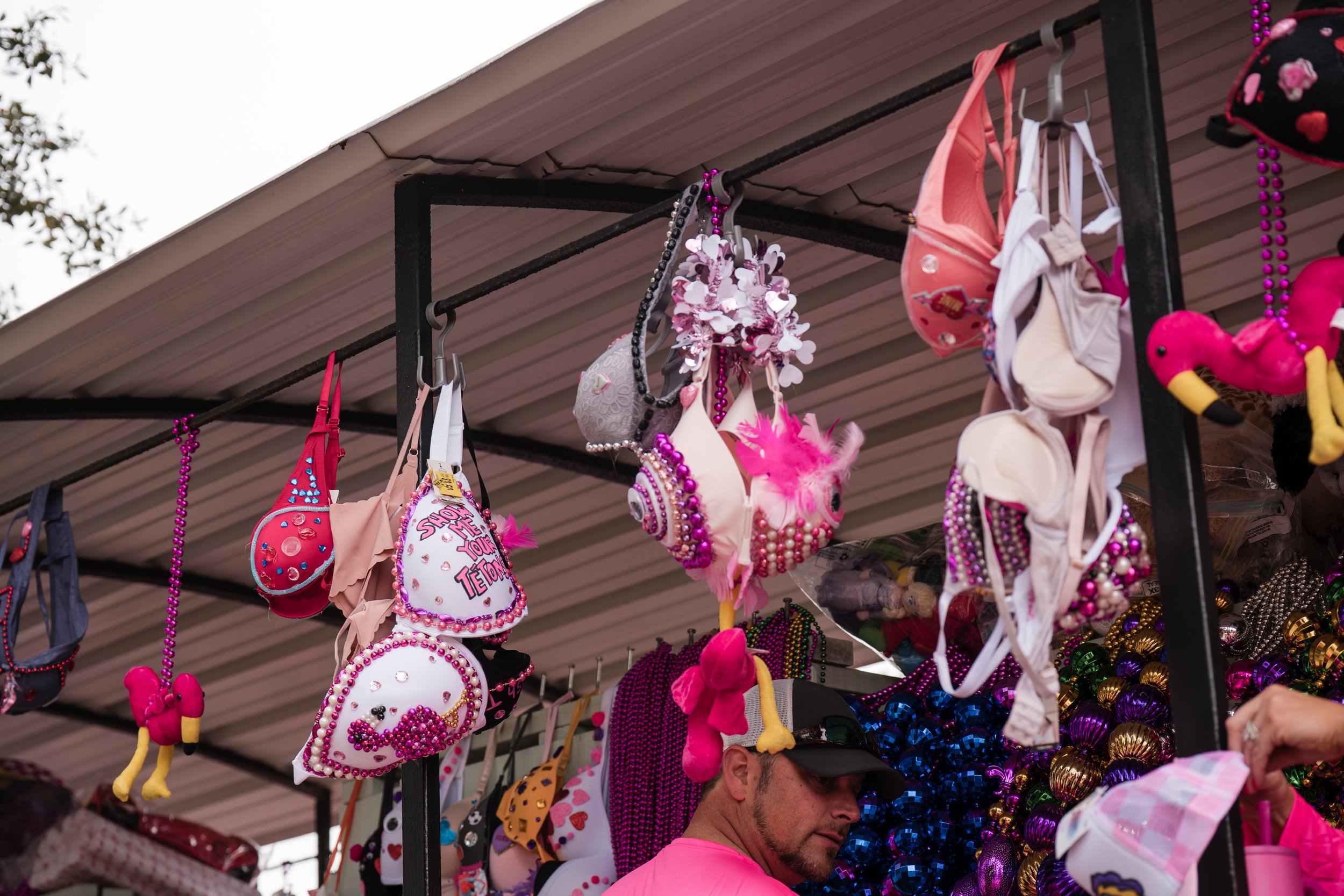 Street vendor stall selling colorful, novelty purses, handbags, and accessories decorated with beads, feathers, and plush toys at an outdoor market.