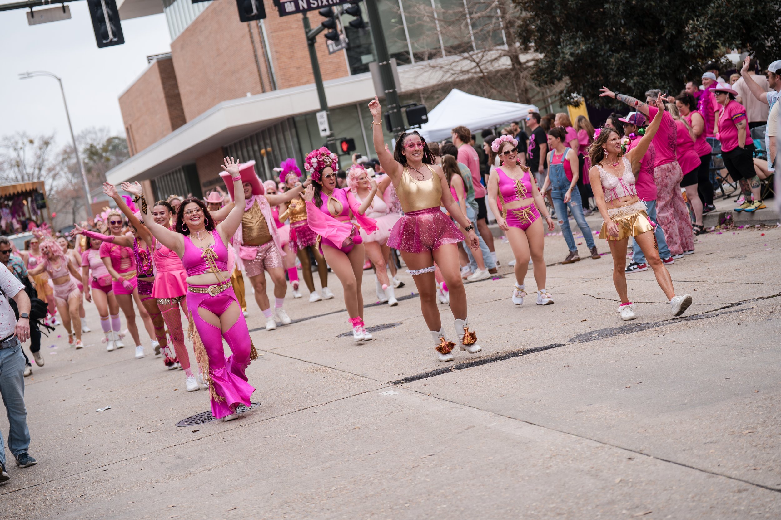 People participating in a parade, wearing pink and gold costumes, skating, and dancing in the street.