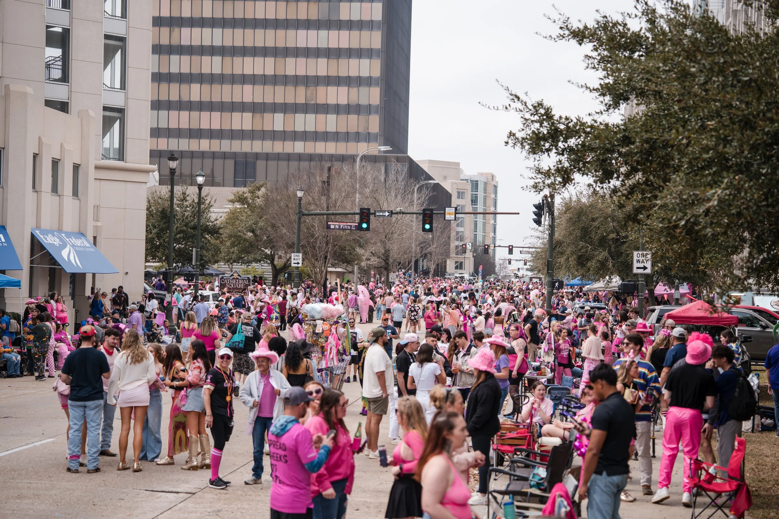 Crowd of people participating in a large outdoor pink-themed event, many dressed in pink clothing and accessories, gathered in an urban street.