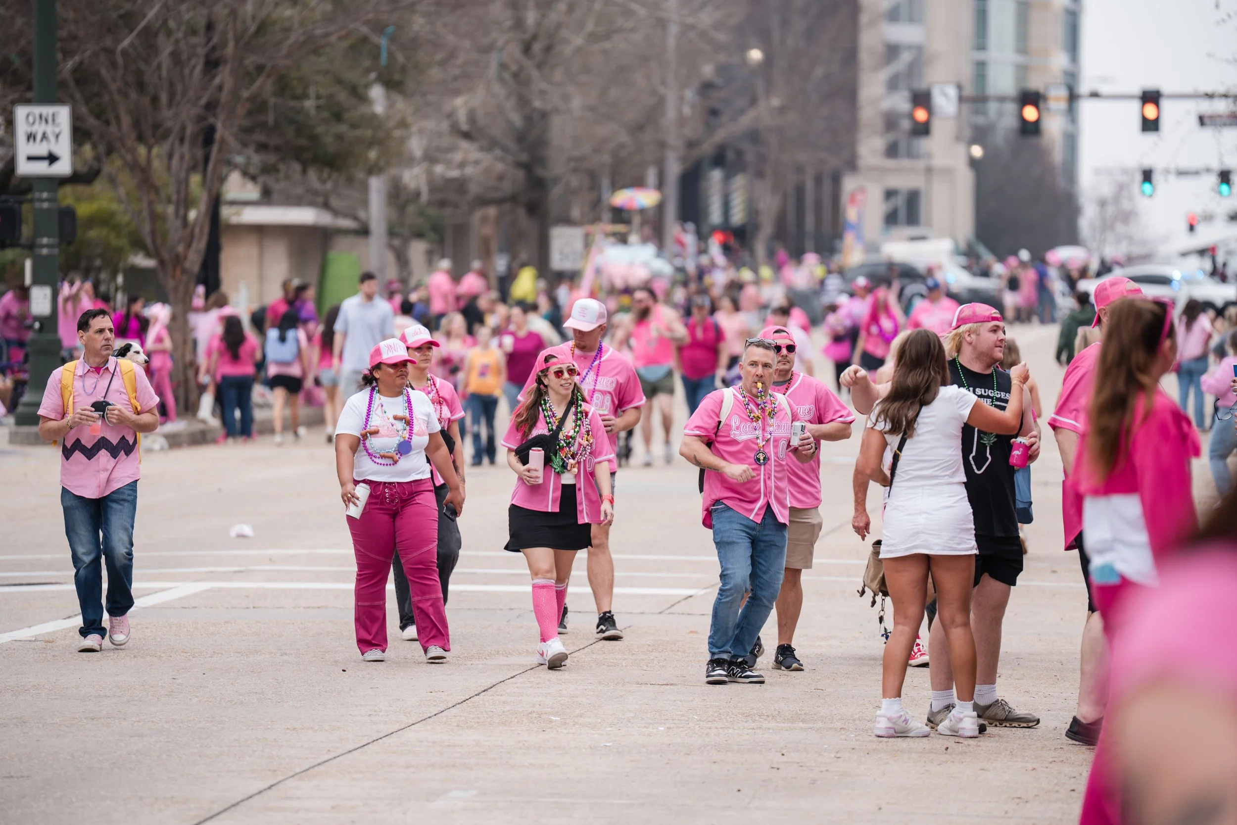 People walking and gathering outdoors, many dressed in pink, in a city street.