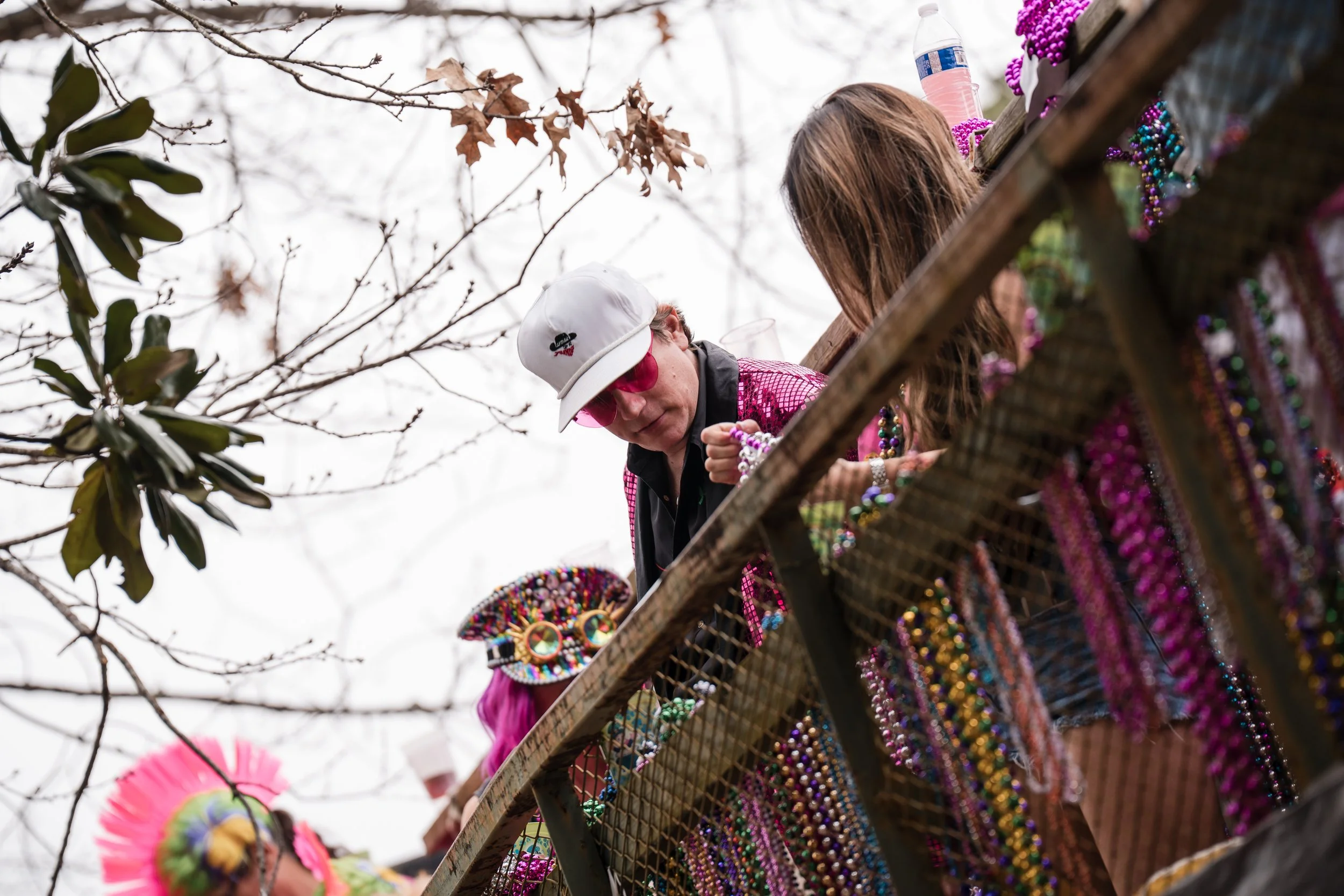 People dressed in colorful, beaded costumes on a parade float decorated with beads, jewelry, and accessories, with a person handing out items.