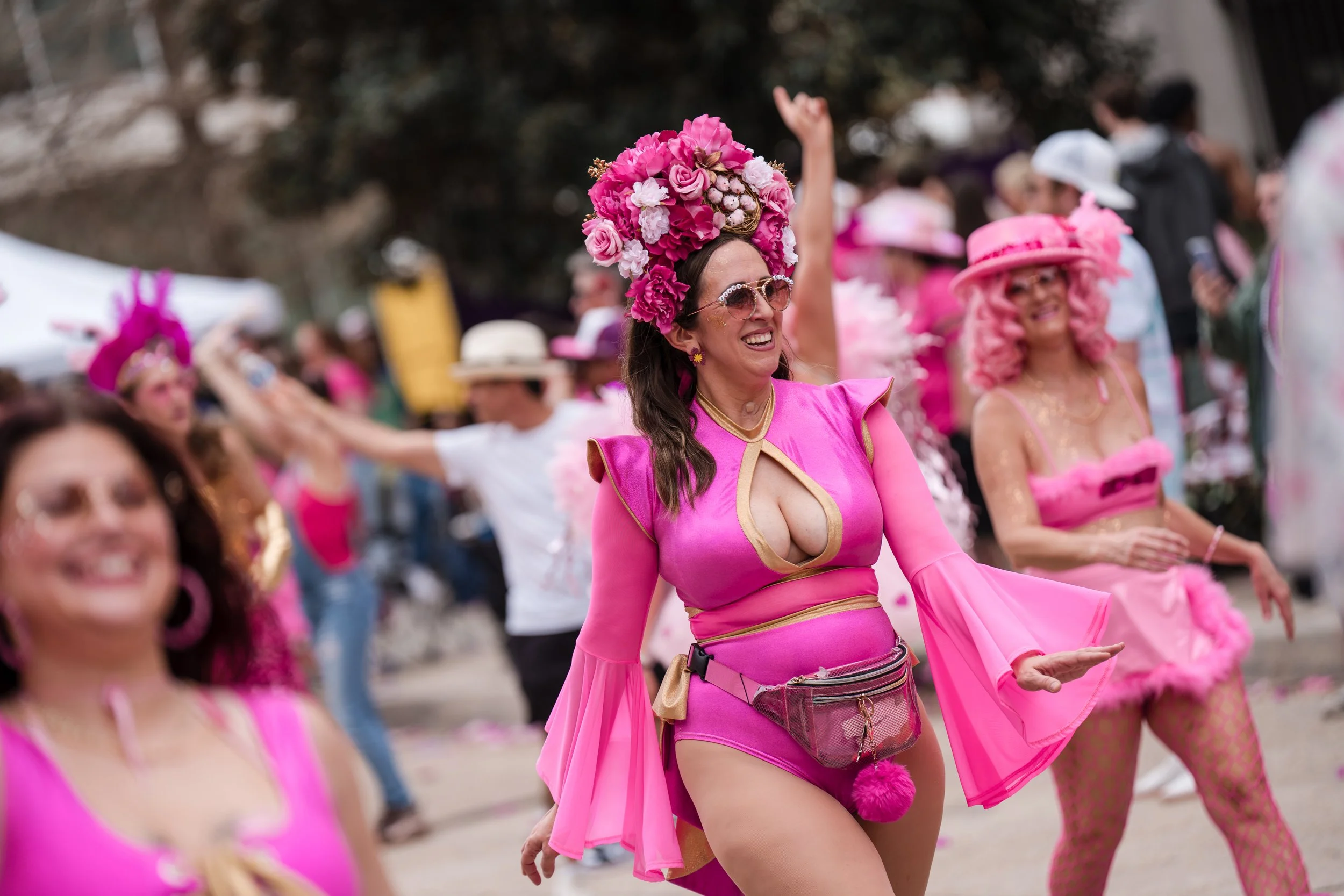 Women dressed in bright pink costumes with floral headdresses dancing at an outdoor event.