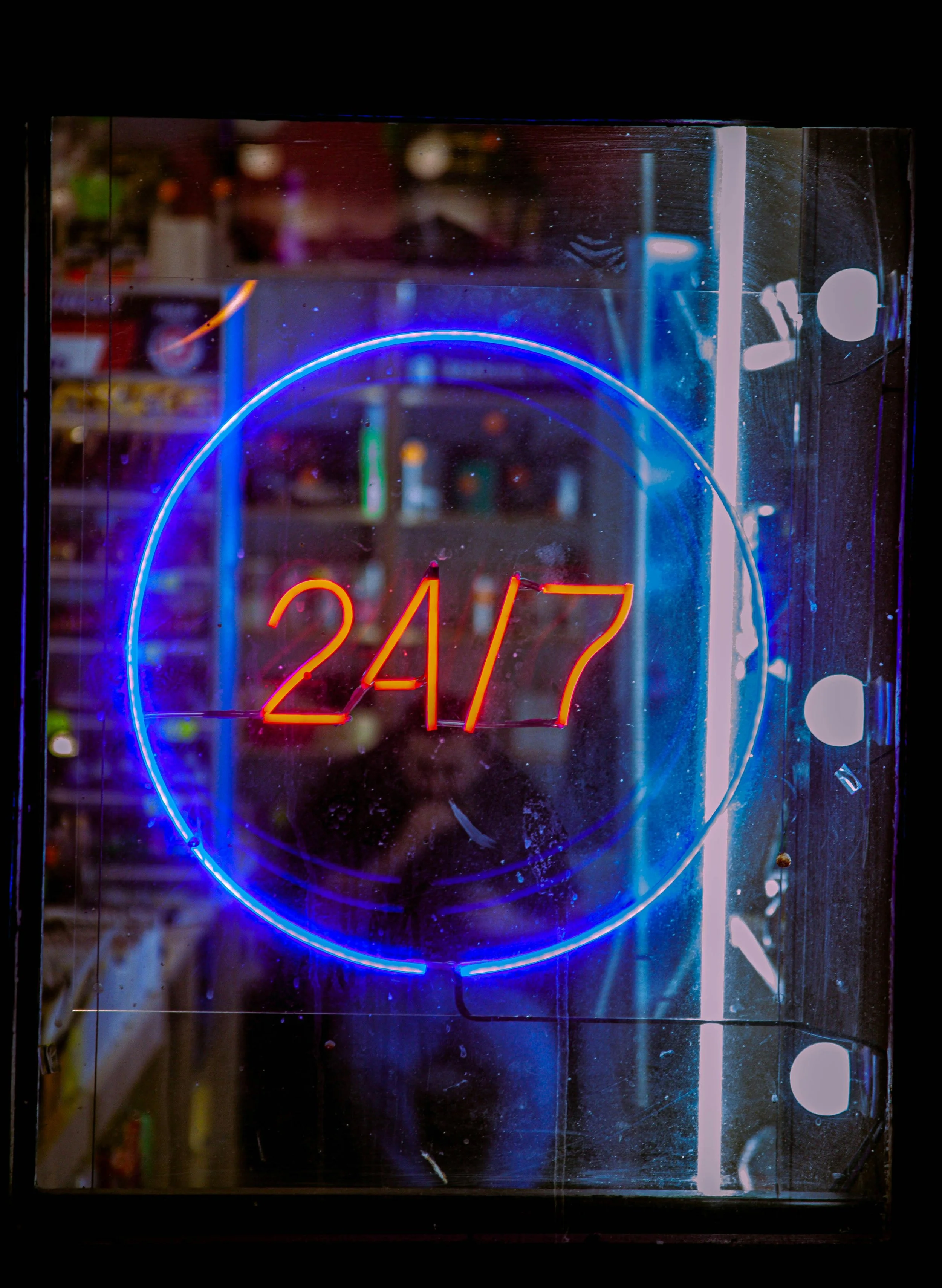 Neon sign displaying '24/7' in red inside a blue circle, indicating 24-hour service.