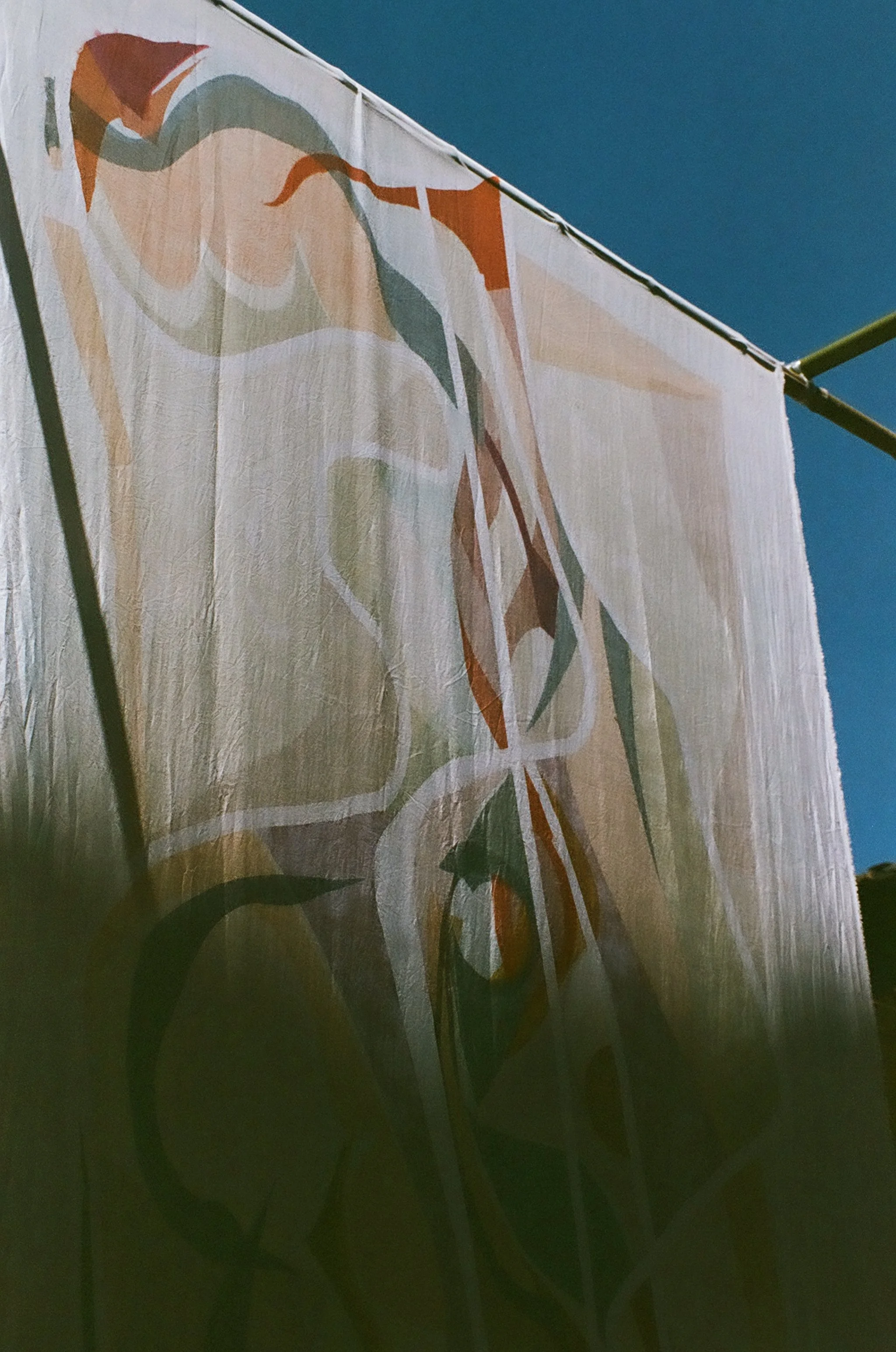 Close-up of a white fabric banner with colorful abstract floral designs, viewed from below against a blue sky.