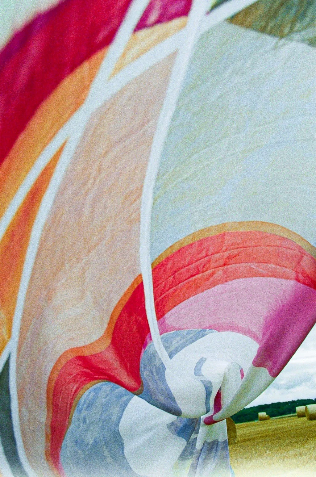 Close-up of a large, colorful abstract painting or mural featuring curved shapes and pastel colors, set against a rural landscape with hay bales in the background.