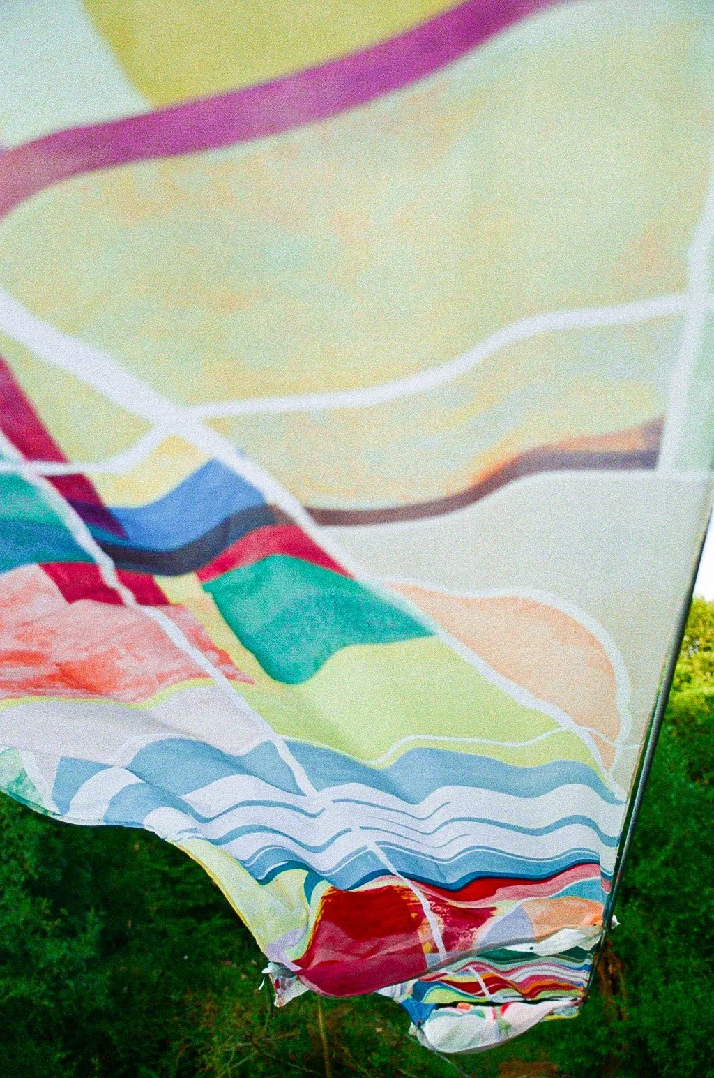 Colorful beach umbrella with various bright sections, set outdoors on a grassy area.