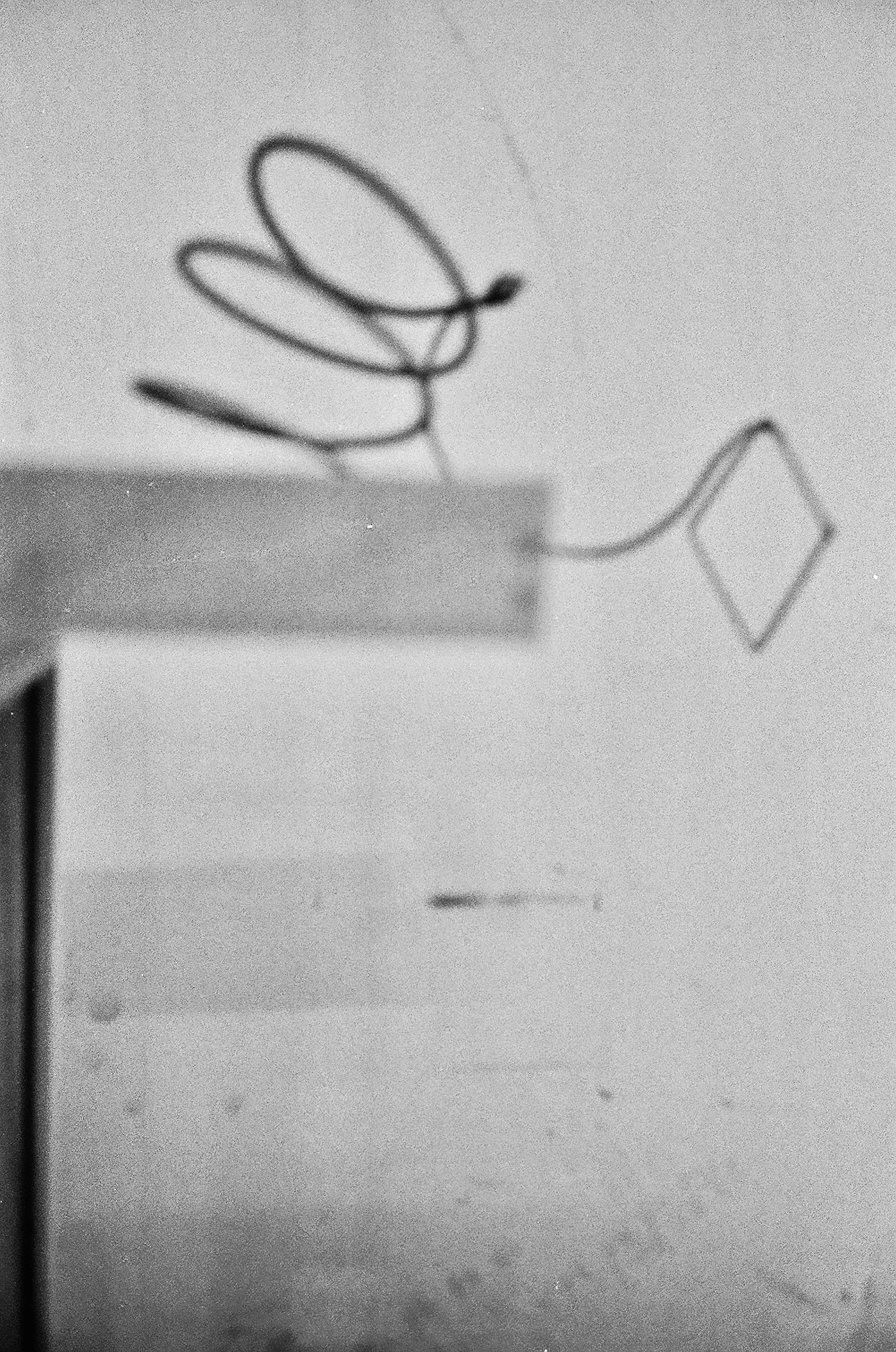 Close-up of a single curly metal paperclip reflected on a light-colored surface.