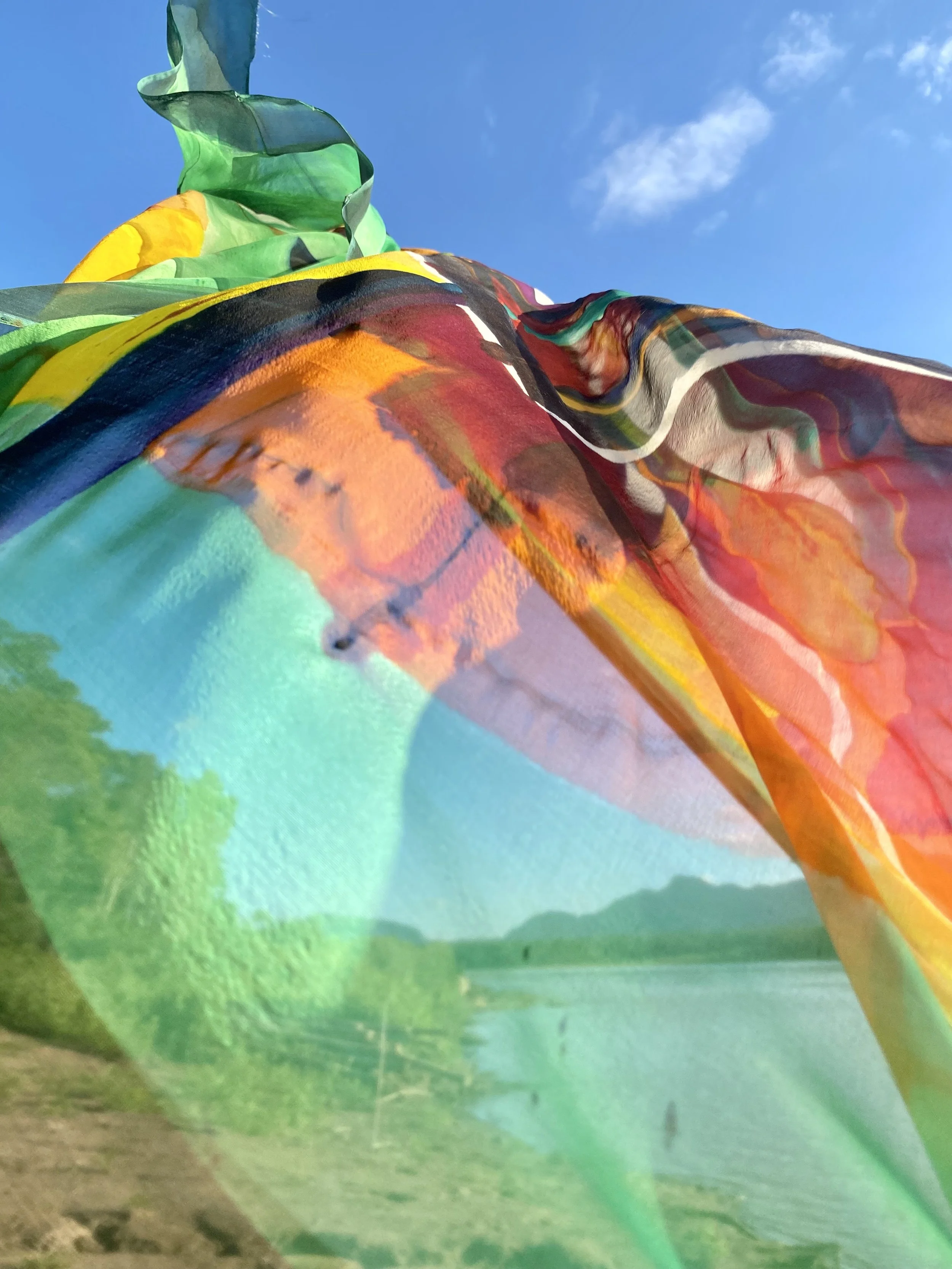 Close-up of colorful, patterned fabric or material with folds, against a bright blue sky with a few white clouds.
