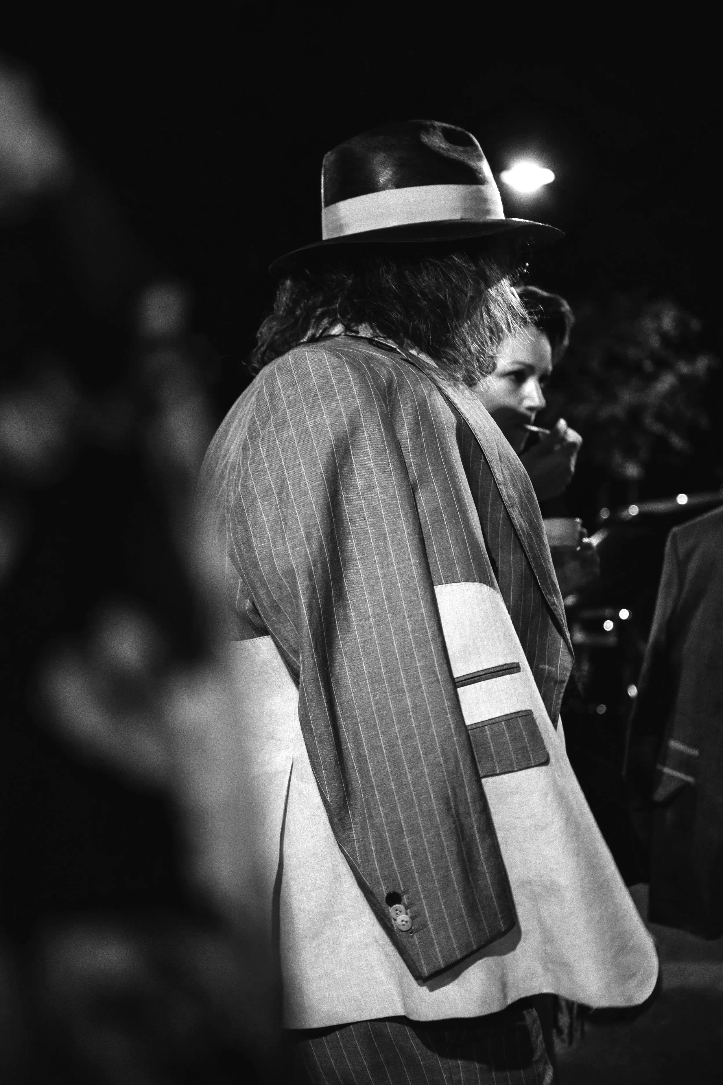 Una persona con cappello e giacca a righe, vista di lato, in una scena in bianco e nero.