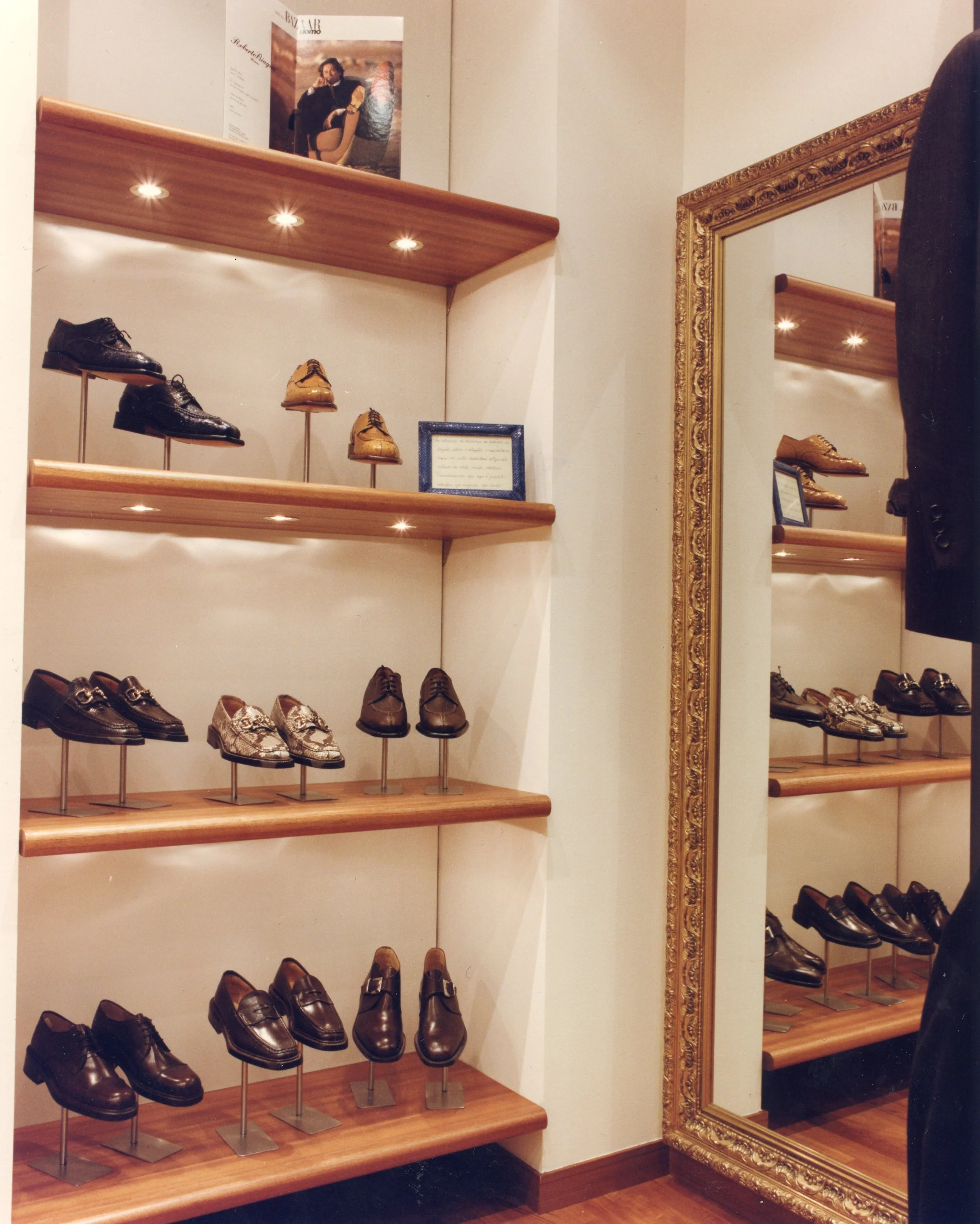 Scarpiera con scarpe da uomo di vari modelli e colori, riflessa in uno specchio con cornice dorata.