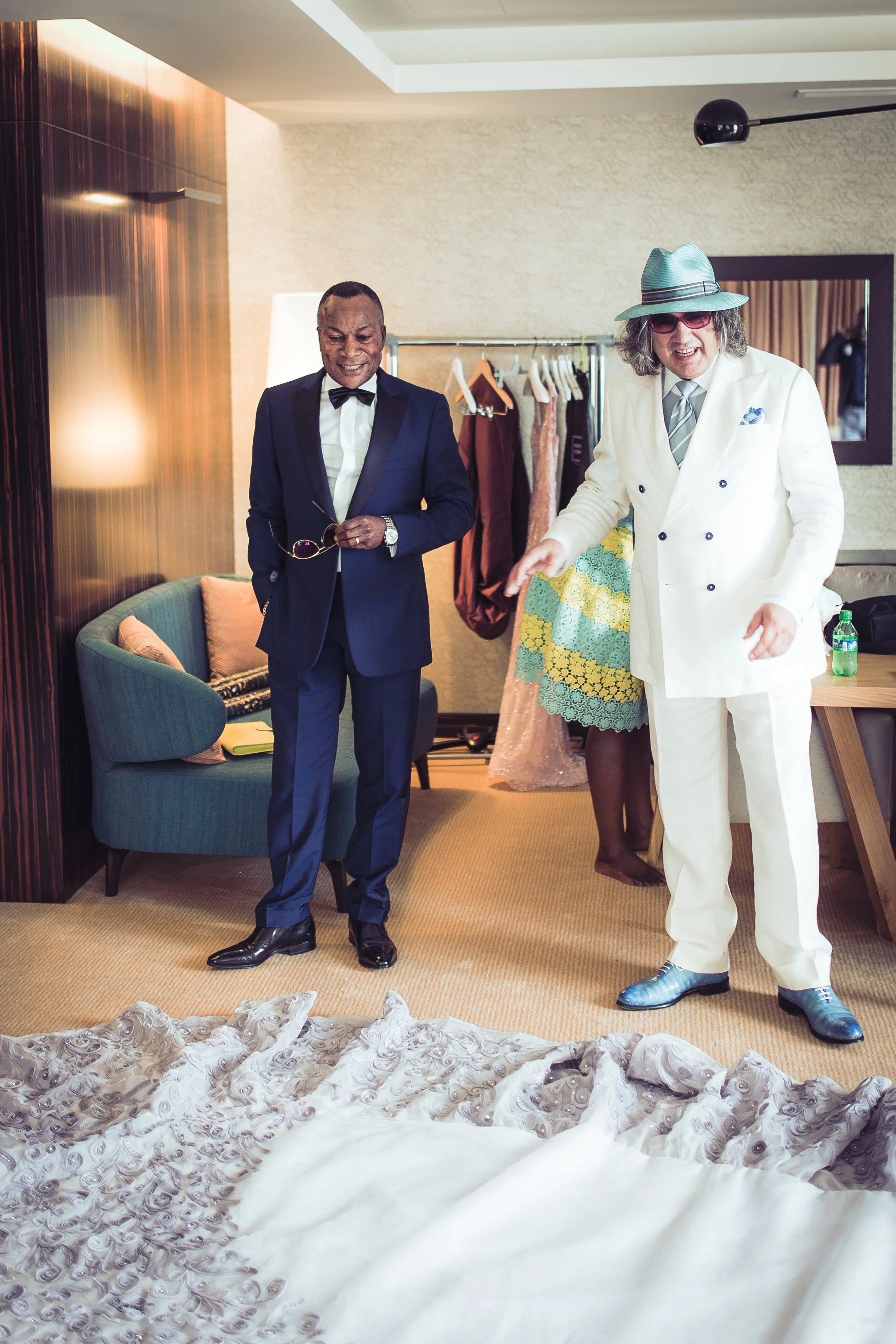 Due uomini in abiti eleganti stanno osservando un vestito da sposa su una superficie in primo piano.