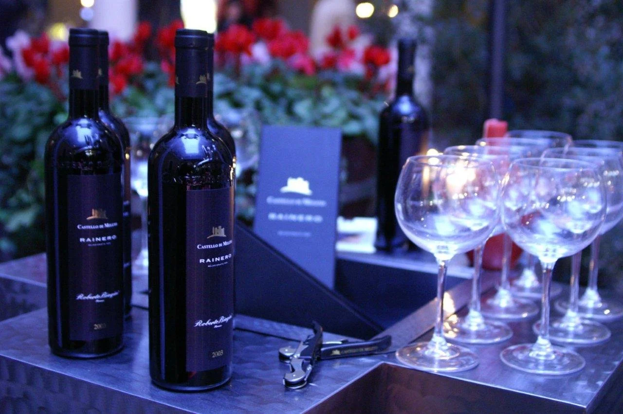 Bottiglie di vino rosso, bicchieri da aperitivo vuoti e cacciavite su un tavolo, sfondo di piante e luci soffuse