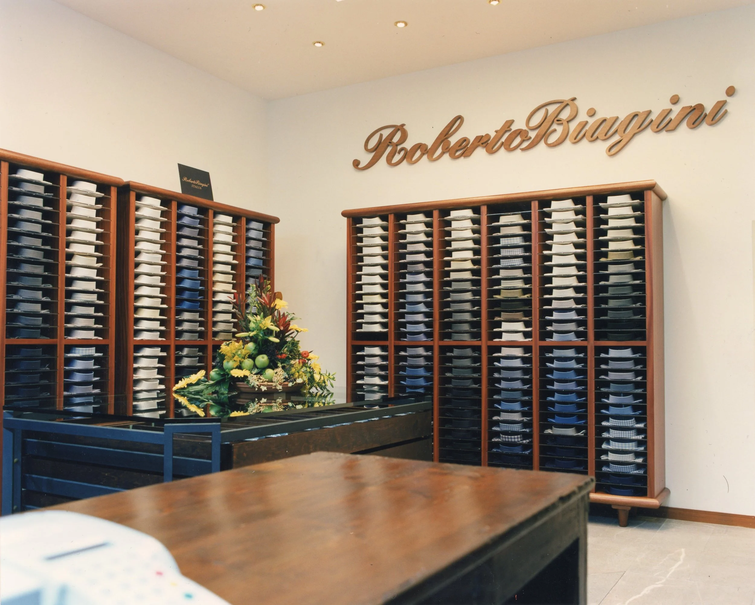 Interno di una sartoria con scaffali pieni di pezzi di tessuto di vari colori e un tavolo con decorazioni floreali