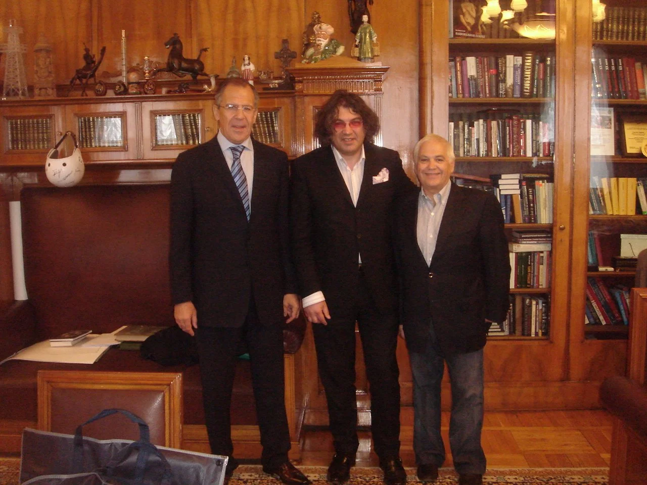 Tre uomini in abiti formali che posano in una stanza con pareti di legno e scaffali pieni di libri.